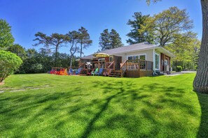 Una casa pequeña con terraza, rodeada de césped cuidado y árboles.