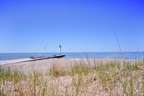 A coastal scene with a lighthouse, a pier extending into the water, and grassy dunes.
