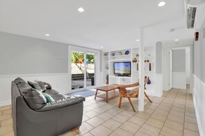 Una sala moderna con un sofá de cuero gris, una mesa de centro de madera y un televisor sobre una pared blanca.