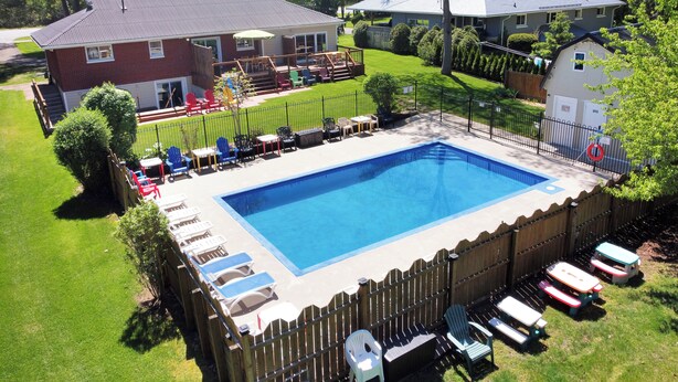 A rectangular swimming pool surrounded by a wooden fence, with lounge chairs and tables arranged around it.