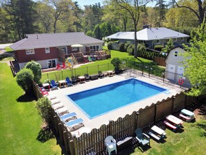 A rectangular swimming pool surrounded by a wooden fence, with lounge chairs and tables arranged around it. - Grand Bend Pool Cottage | Groups Welcome | Firepit & Huge Yard | Beach 2km (Grand Bend)