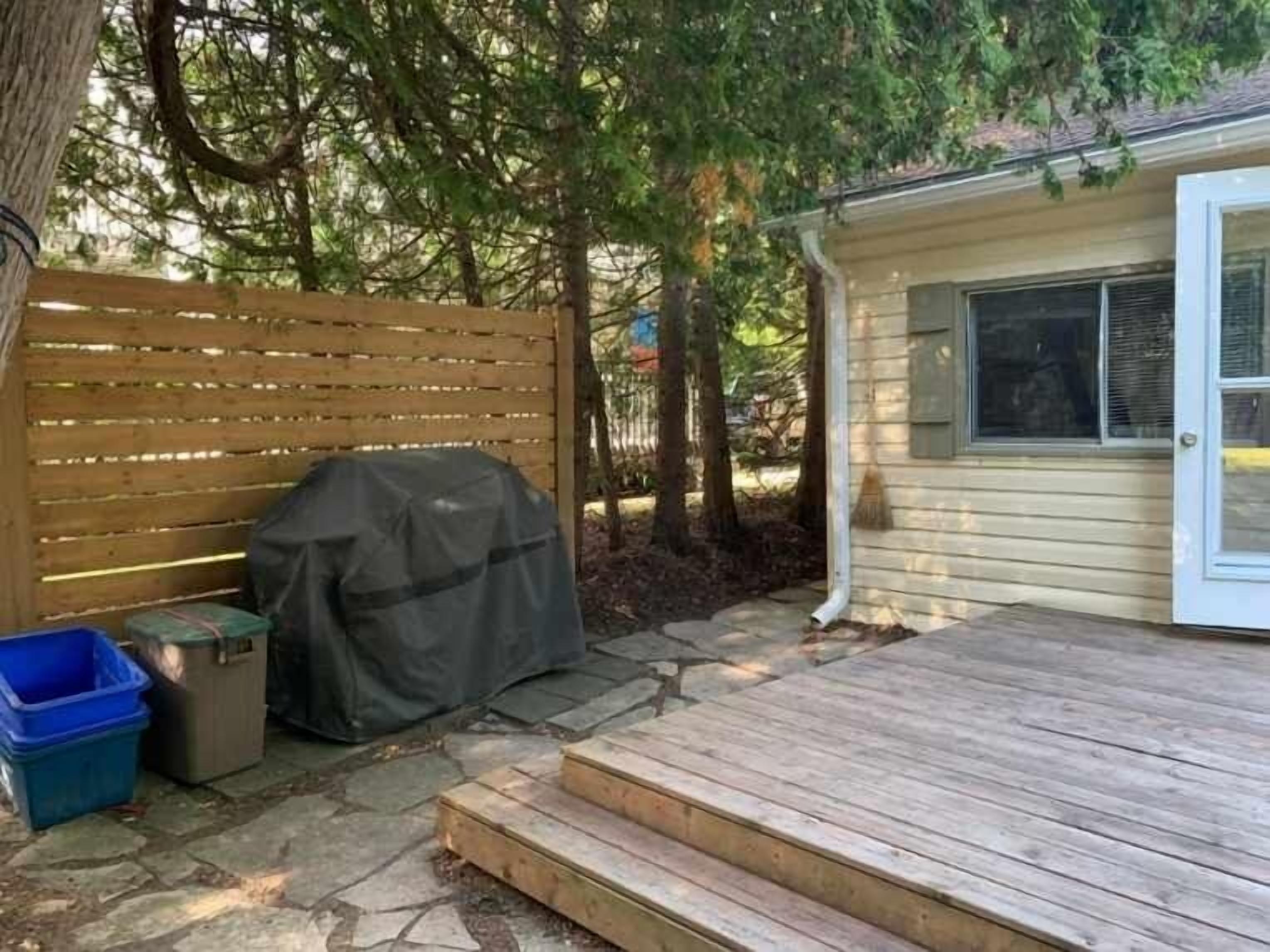 Eine Holzterrasse mit Stufen zu einem überdachten Grillbereich, einem Mülleimer und einer blauen Aufbewahrungsbox.