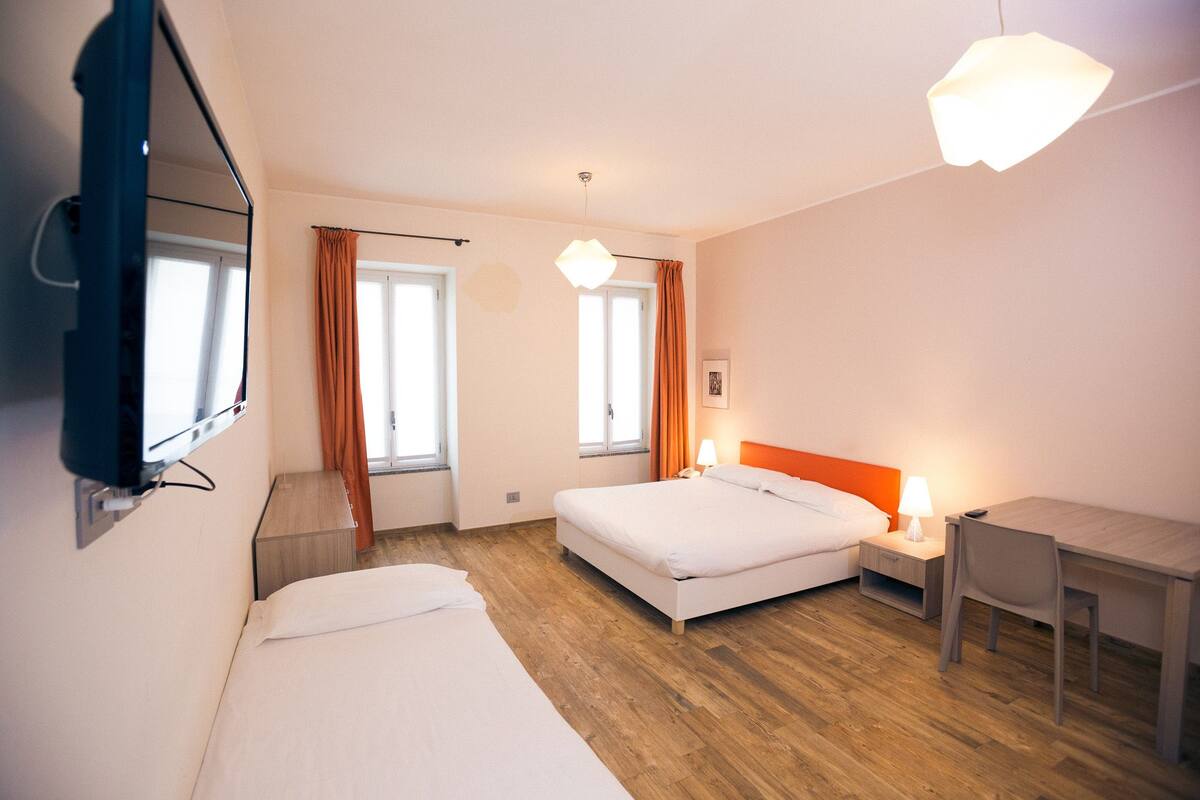 A hotel room with a bed, bedside table, lamp, and a desk.