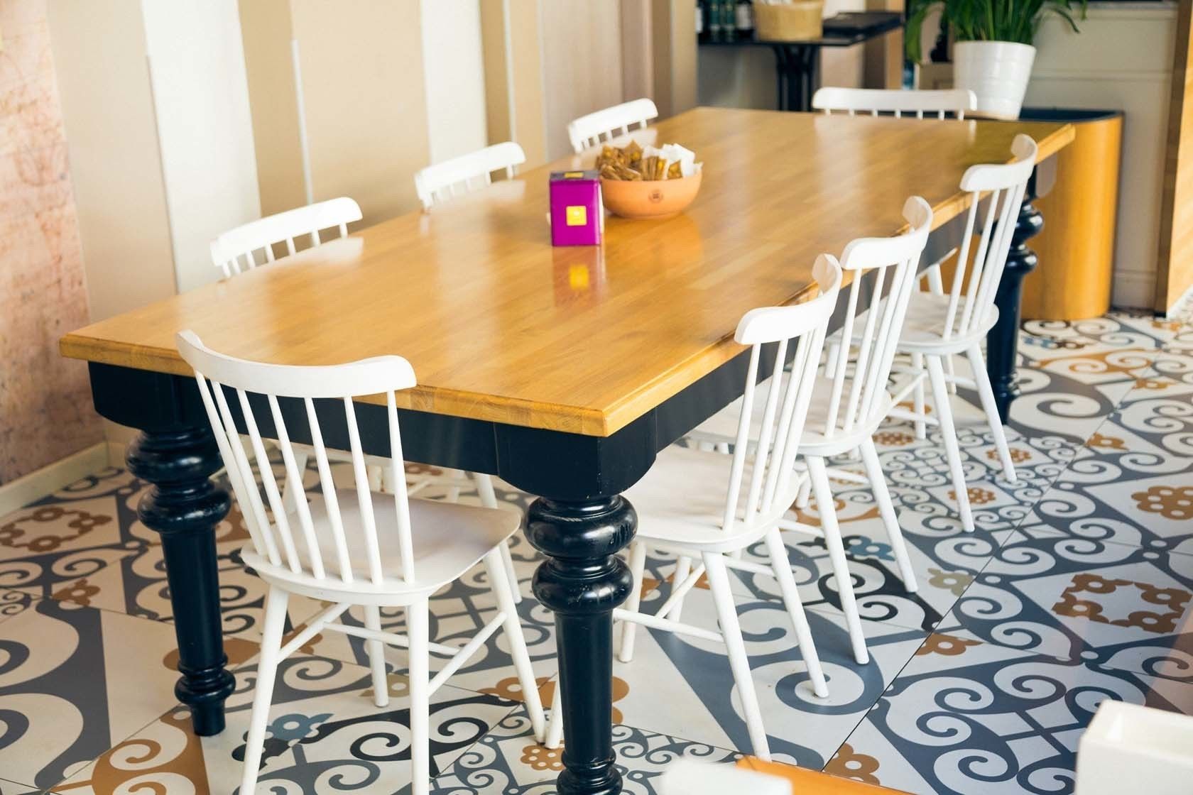 Un comedor con una mesa de madera y sillas blancas, un cuenco de aperitivos y un piso con diseño.