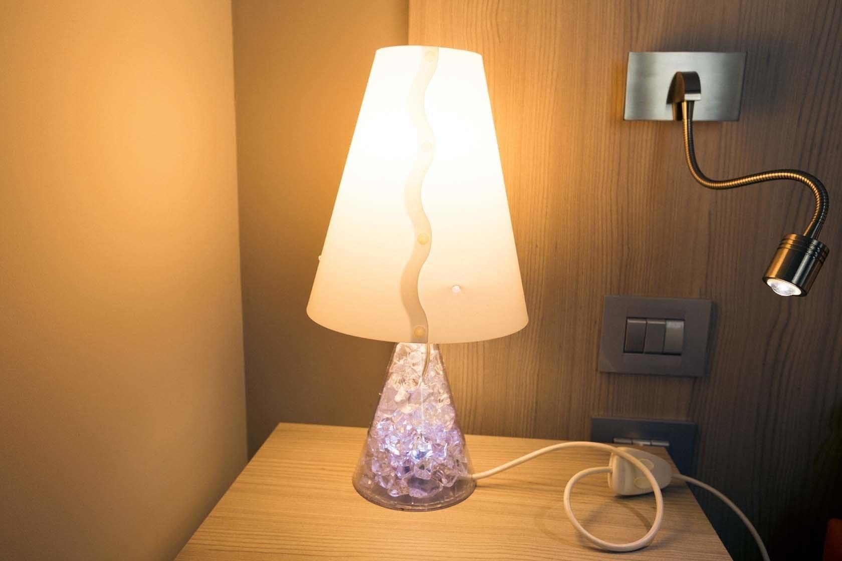 Uma luminária de mesa com um abajur ondulado e peculiar, ligada a uma tomada em uma superfície de madeira.