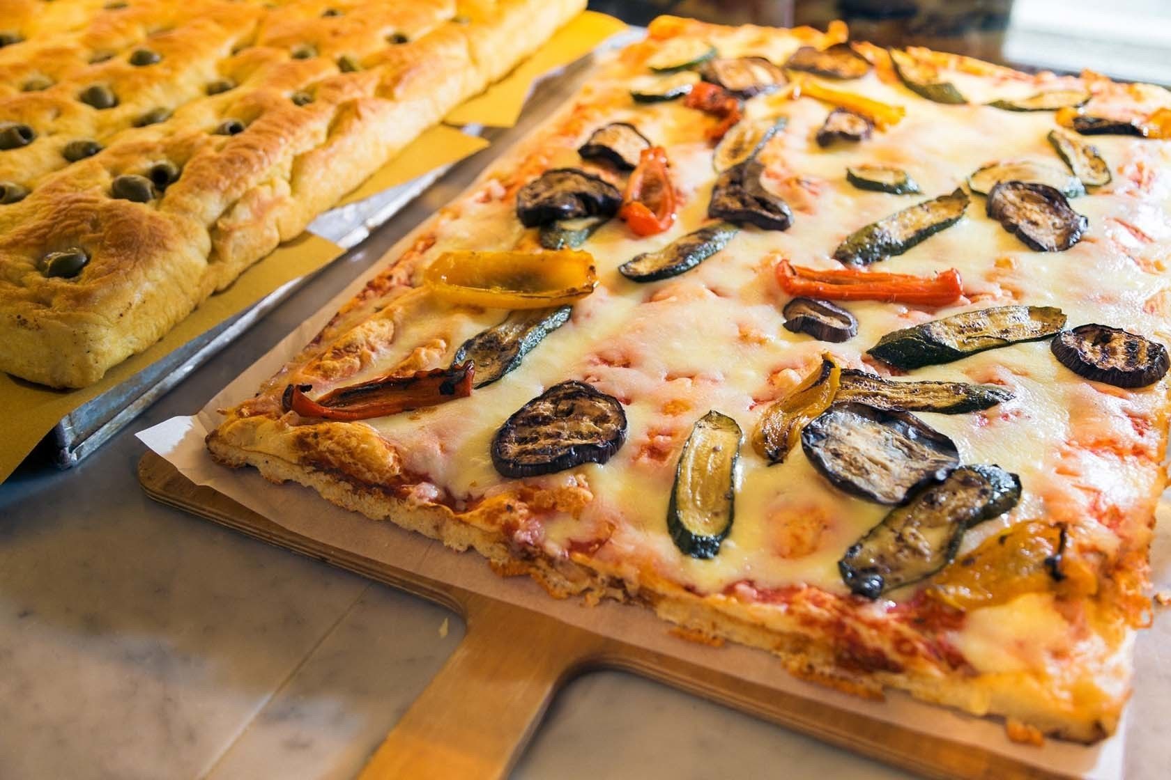 Pizza mit verschiedenen Belägen, darunter Gemüse und Käse, auf einem Holzbrett serviert.