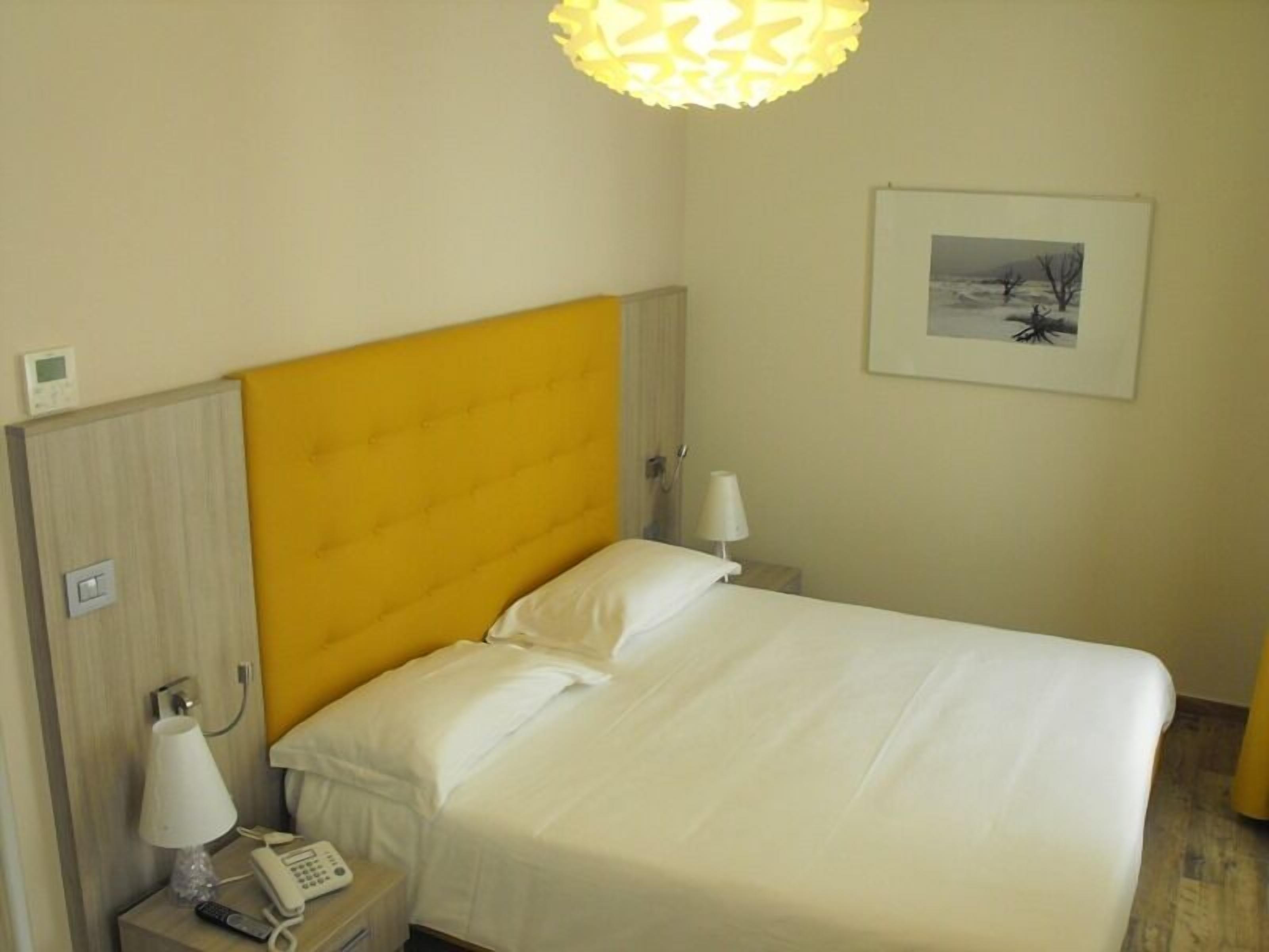 A hotel room with a bed, bedside lamps, a phone, and a painting on the wall.