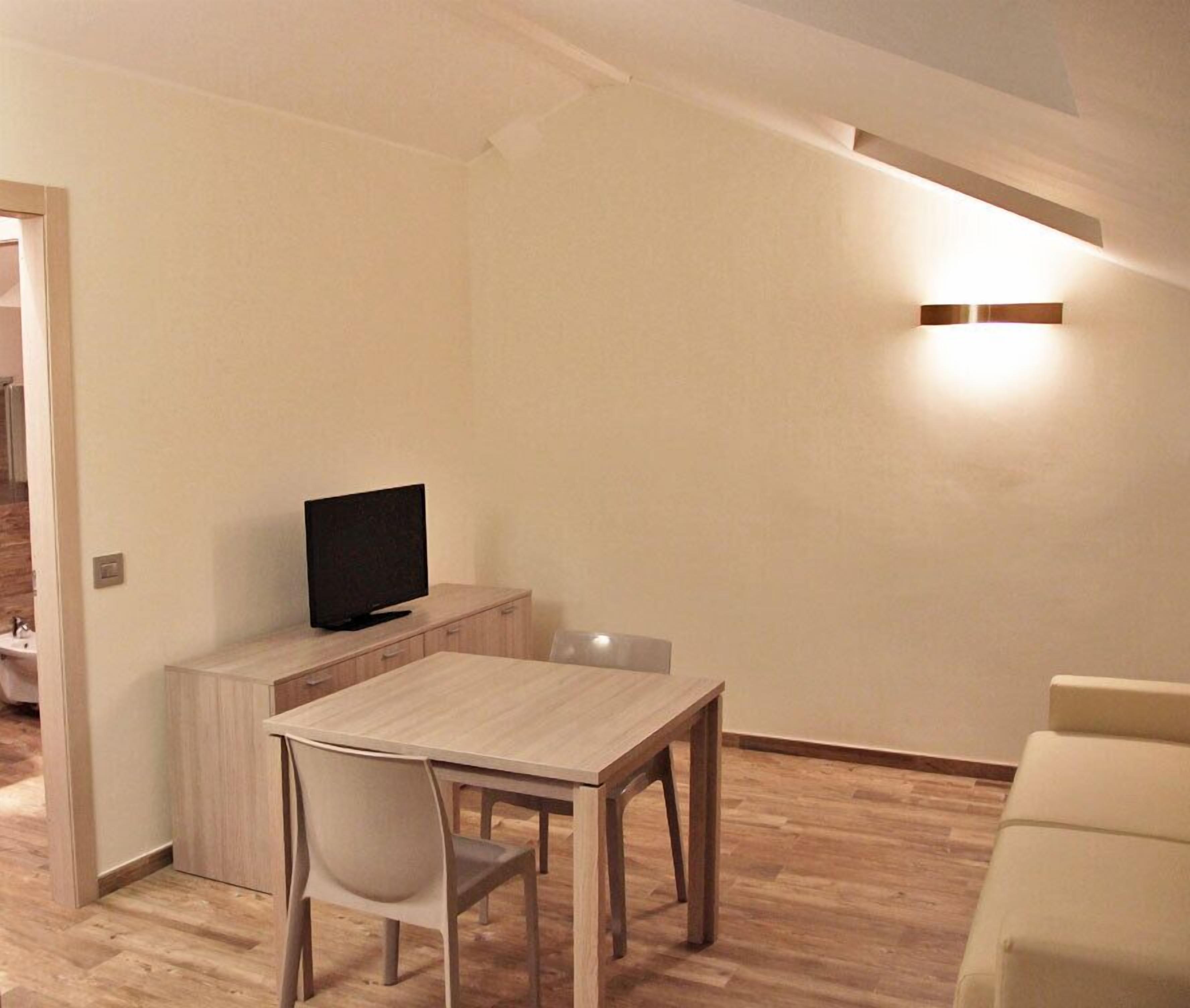 A compact living space with a wooden dining table, a TV on a low cabinet, and a sofa.