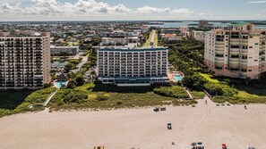 Een hoog hotel met meerdere verdiepingen, een zwembad en een strandgedeelte met parasols.