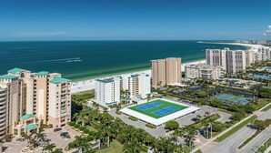 Een hoog hotel met meerdere verdiepingen, een tennisbaan en uitzicht op het strand.