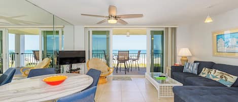 Uma sala de estar moderna com televisão, mesa de jantar e área de estar, com uma varanda e vista para o oceano.