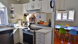 Une cuisine moderne avec des meubles blancs, un four encastré et un coin repas agrémenté de chaises colorées.