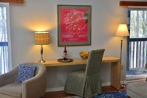 Een woonkamer met een bank, een stoel, een tafel met een fles wijn en glazen, een schaal fruit en een lijst met een poster aan de muur.