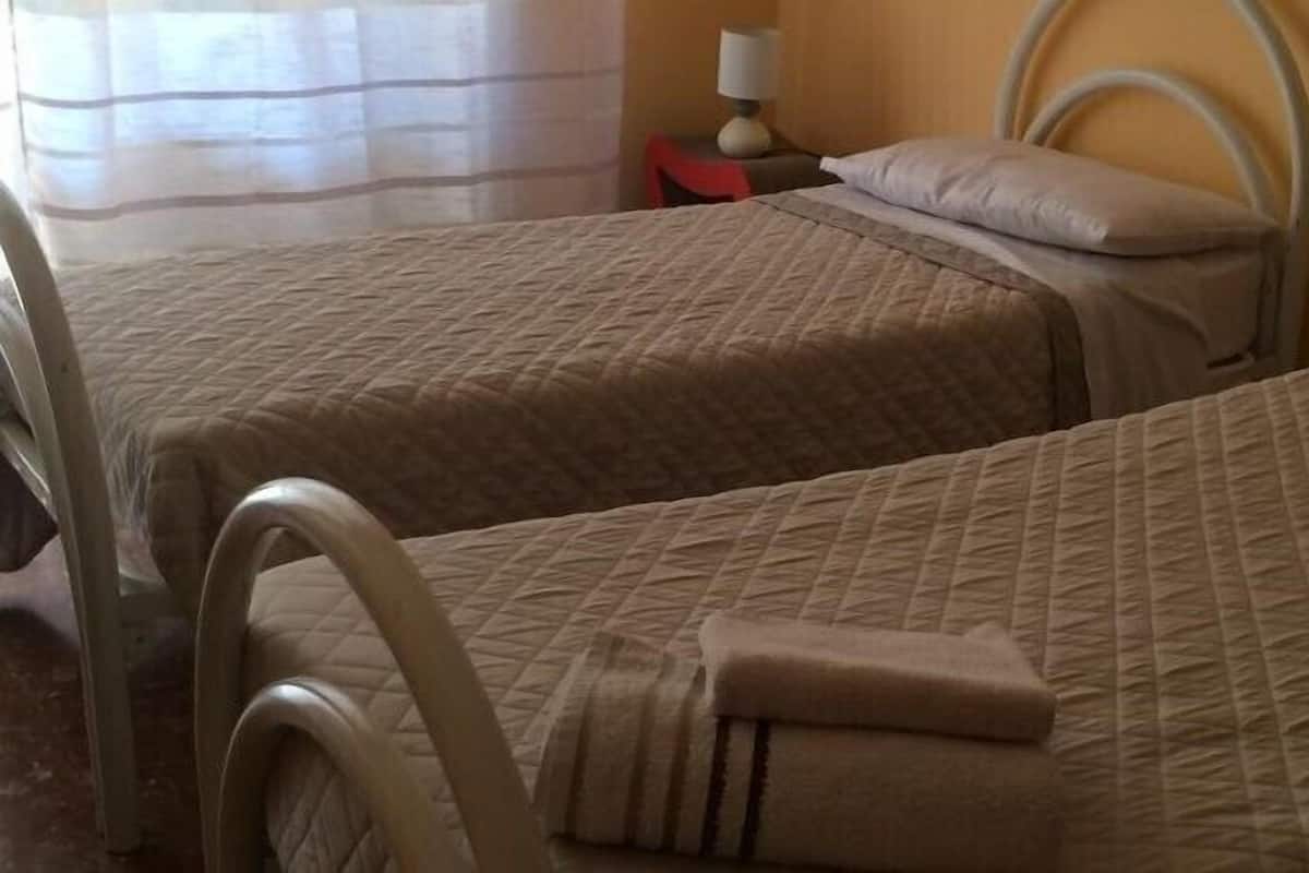 Una habitación con dos camas, cada una con cabecera y almohada. Hay una mesita de noche con lámpara y una silla roja.