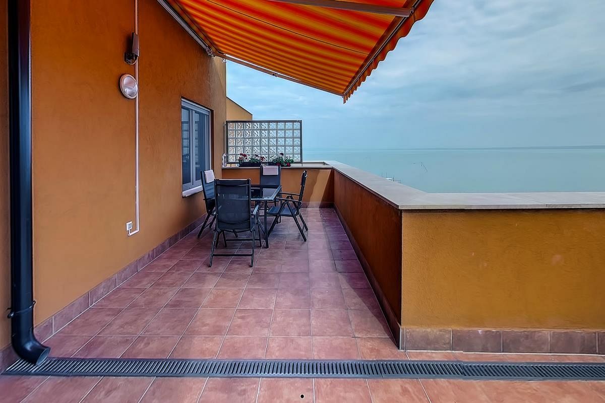 A balcony with a table and chairs, a window with a decorative screen, and a view of the sea.