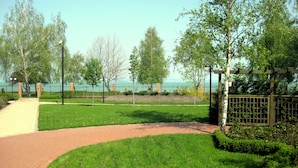 A paved pathway leading to a grassy area with a fence and trees. - Galerius Panorama Beach - D Apartman (Siófok)