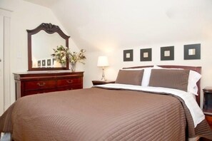 A neatly made bed with a brown quilt, a wooden dresser with drawers, a mirror, and a bedside lamp.