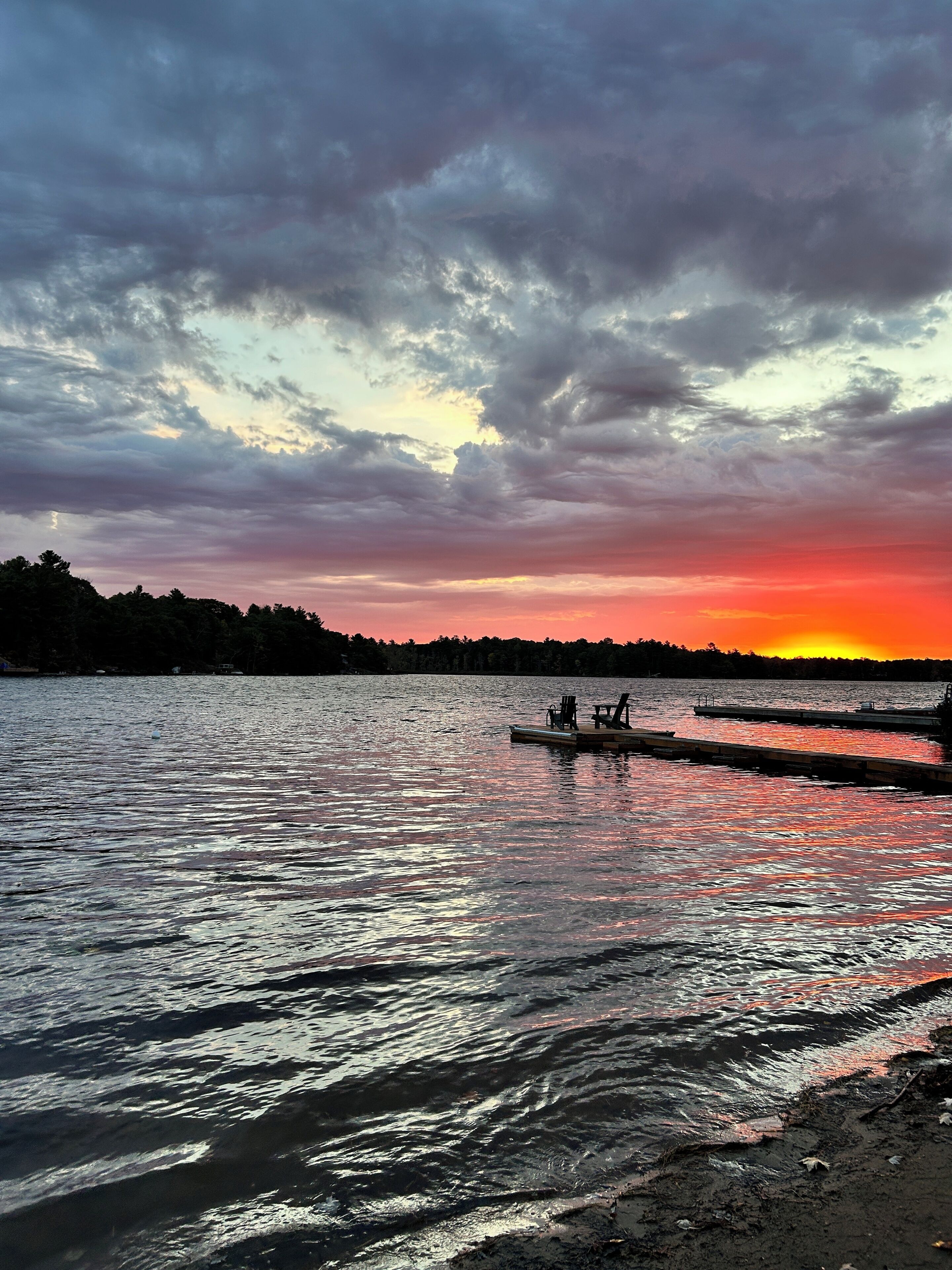 Un atardecer sobre un lago tranquilo, con un embarcadero y un bote.