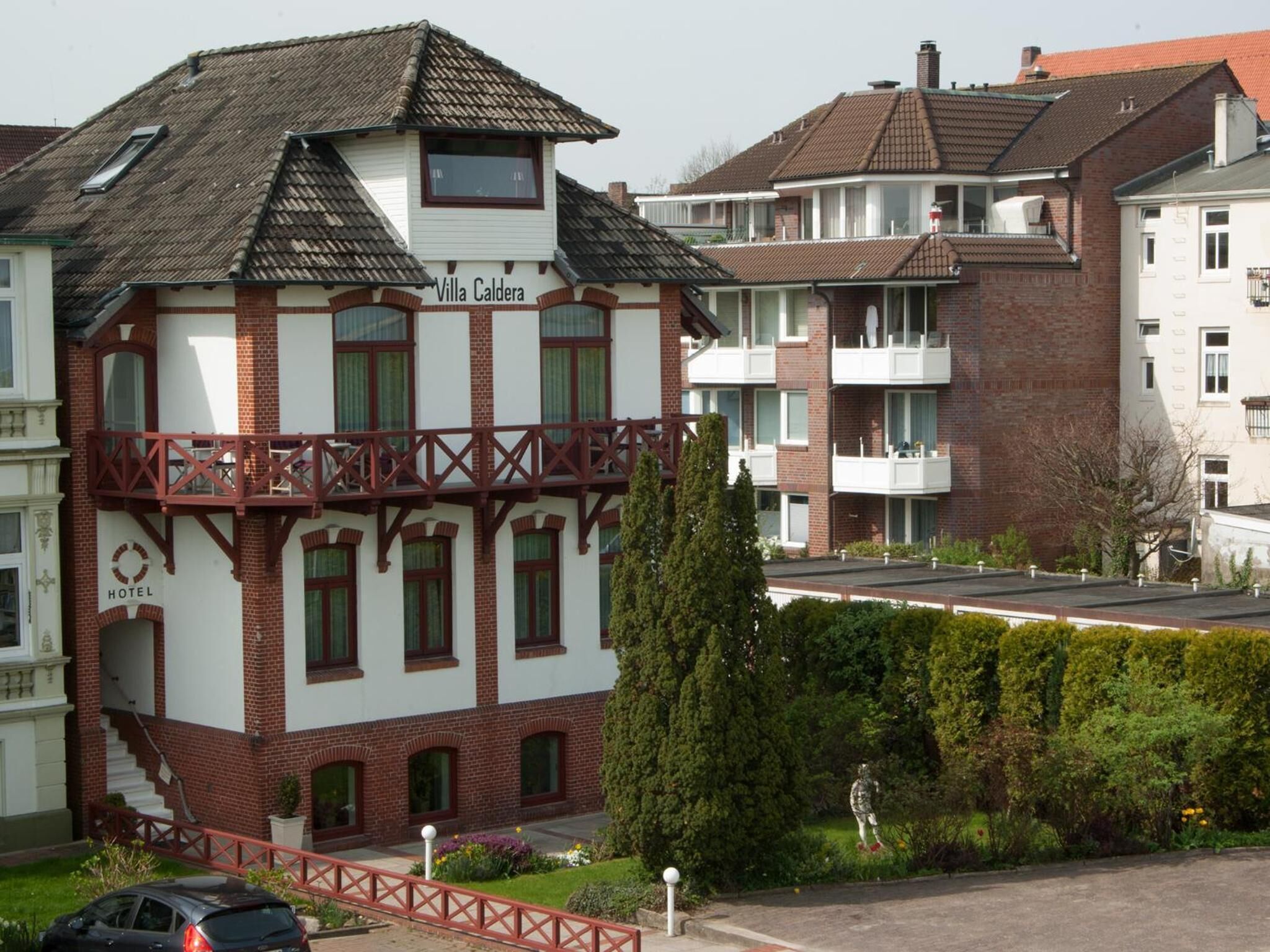 A hotel with a traditional facade, multiple balconies, and a well-maintained garden.
