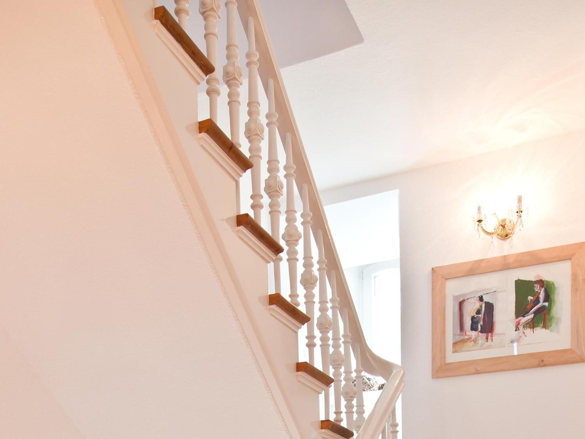 Eine Treppe mit weißen Balustern und Holzdielen, die zu einem Raum mit einer Chandelüstere und einem gerahmten Gemälde an der Wand führt.