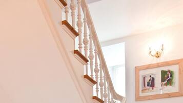 Eine Treppe mit weißen Balustern und Holzdielen, die zu einem Raum mit einer Chandelüstere und einem gerahmten Gemälde an der Wand führt.