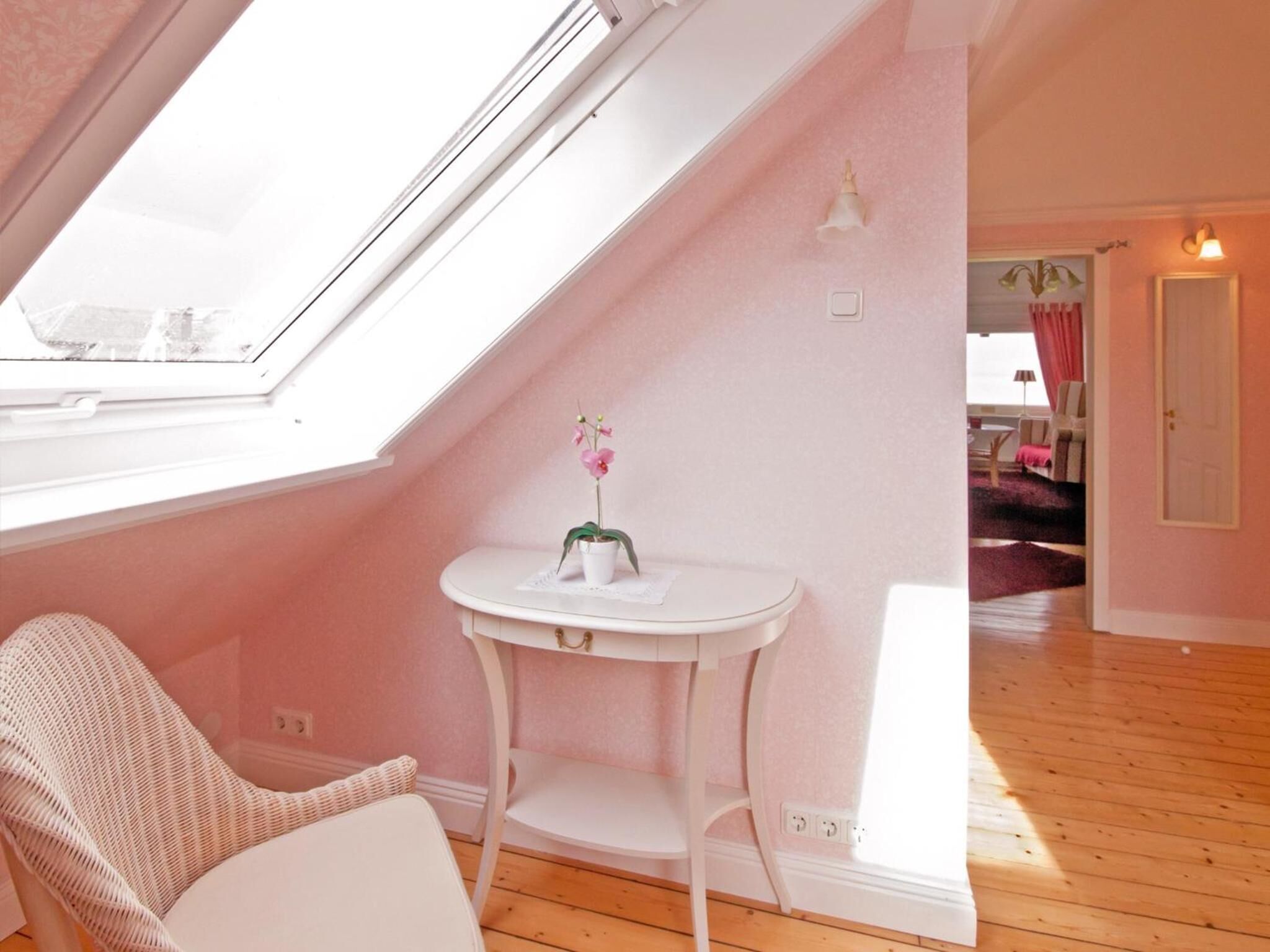 A room with a sloped ceiling, a white chair, a small white table with a potted orchid, and a view through a skylight.