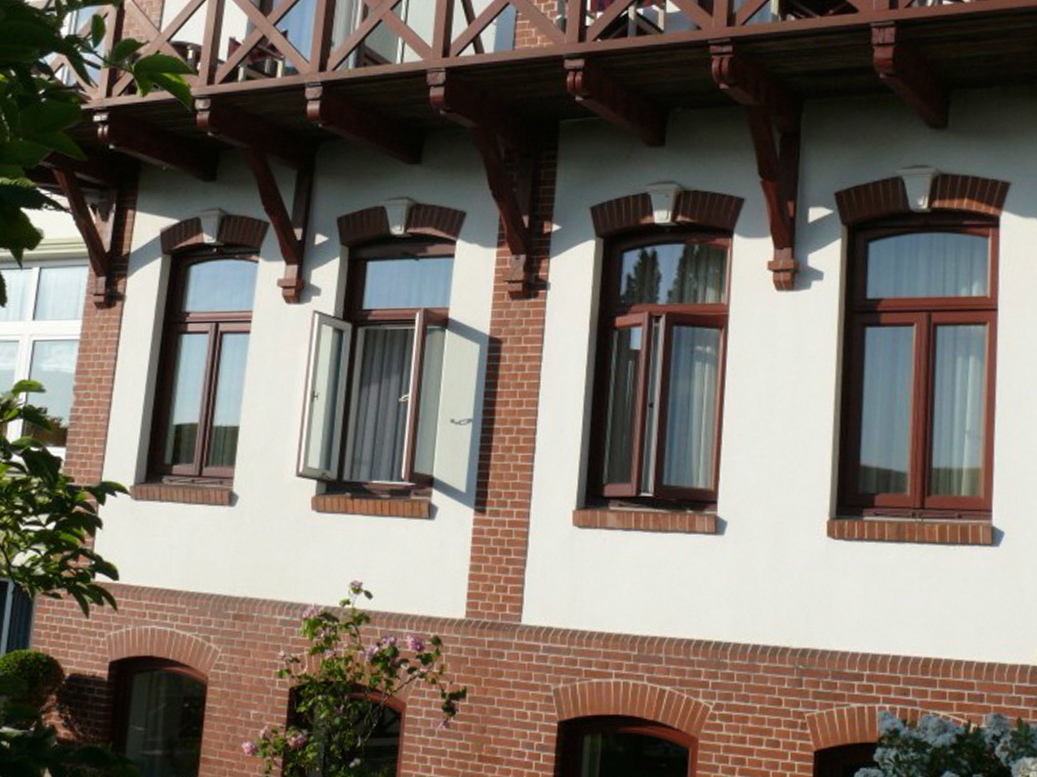 Un edificio con fachada blanca y marcos de ventanas marrones, con varias ventanas y base de ladrillo.