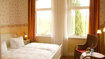 A bedroom with a bed, two bedside tables, a chair, and a window with curtains.