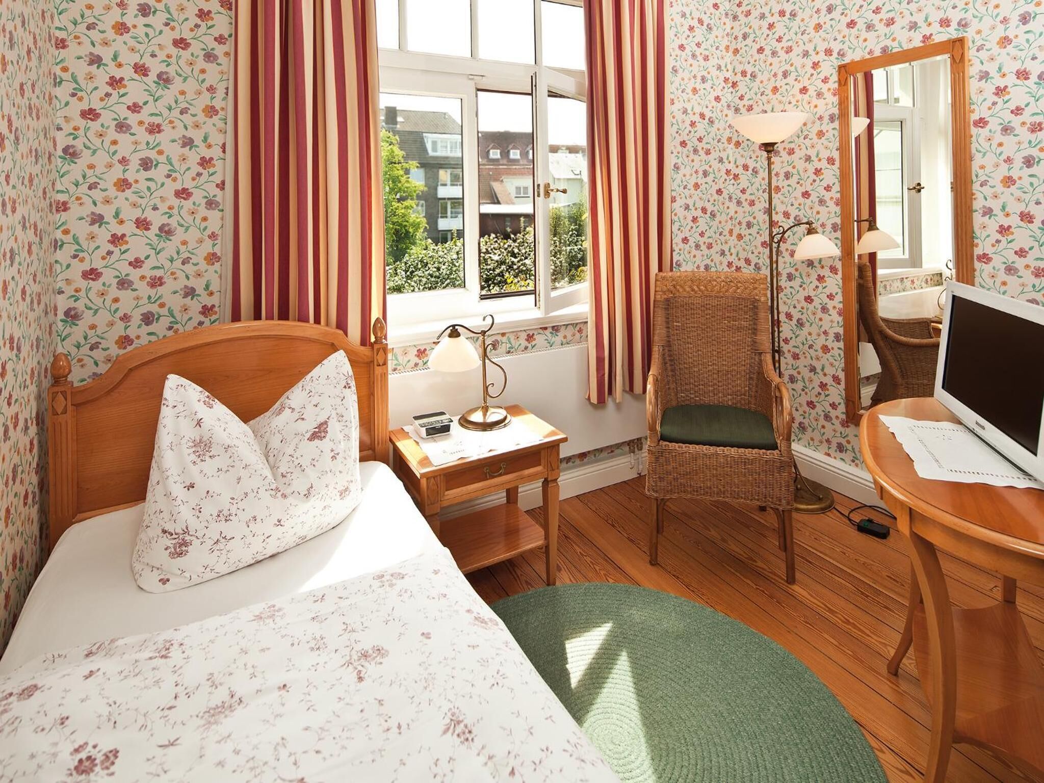 A hotel room with a bed, a chair, a desk with a computer, a lamp, and a window with curtains.