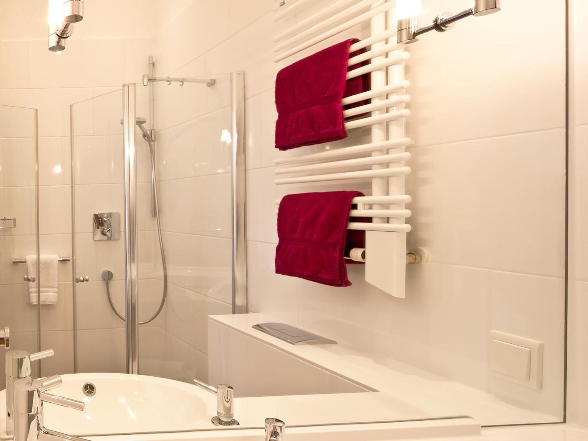 Une salle de bain moderne avec une douche à parois de verre, un lavabo blanc et un sèche-serviettes avec des serviettes rouges.