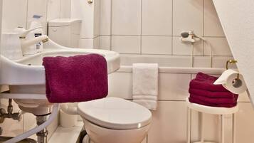 A bathroom with a toilet, sink, and bathtub. There are towels and toiletries visible.