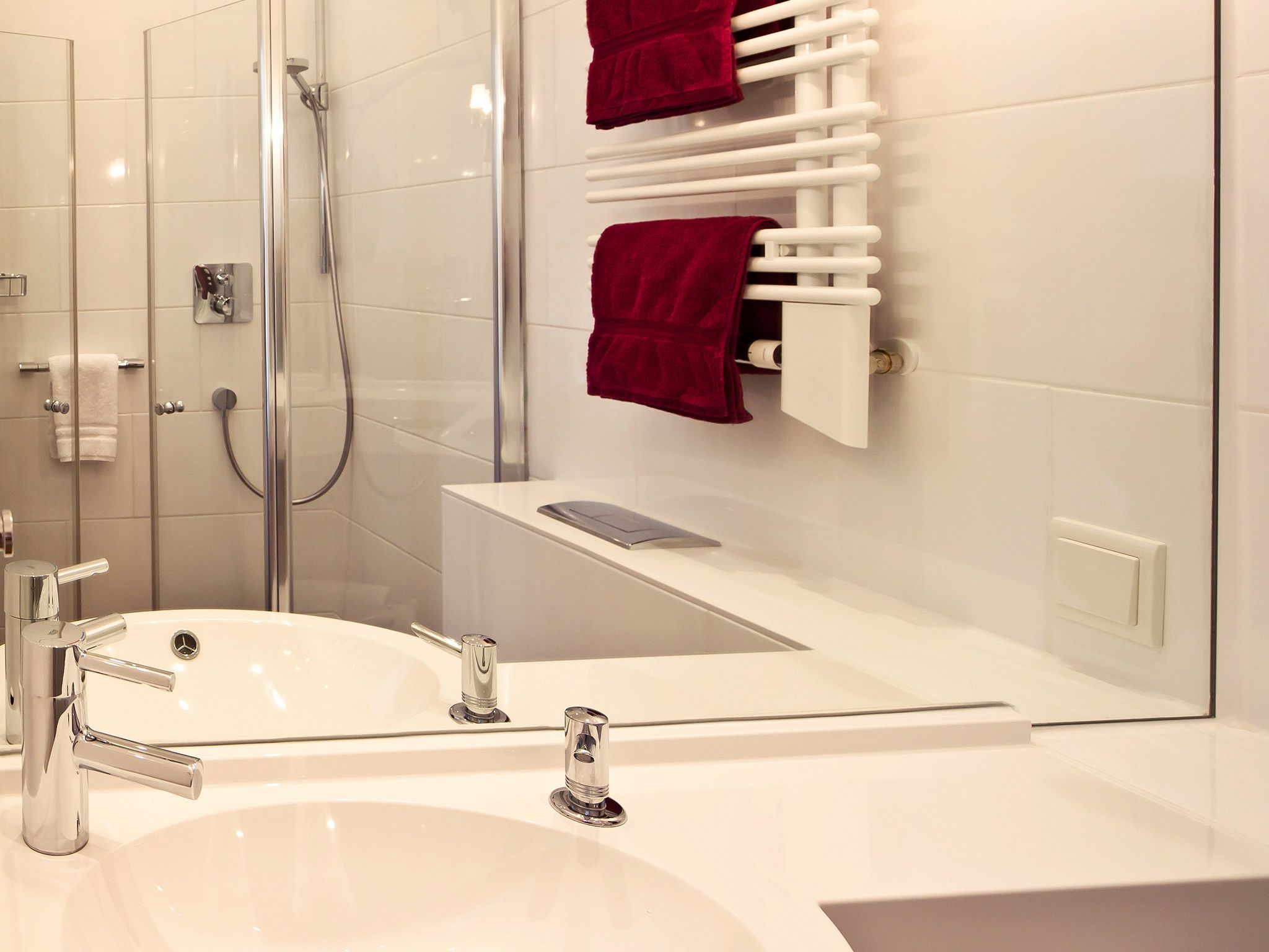 Un bagno moderno con box doccia in vetro, un lavandino bianco con accessori cromati e un portasciugamani con asciugamani rossi.