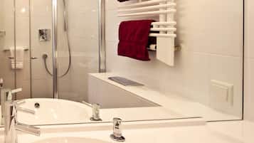 Une salle de bain moderne avec une douche à parois de verre, un lavabo blanc doté de robinetterie chromée et un porte-serviettes avec des serviettes rouges.
