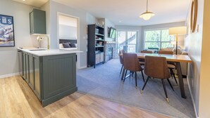 A modern kitchen with a central island, a dining area with chairs, and a staircase leading to an upper level. - Aspens #358 Prime Ski-in Ski-out Location! Pool, Hot tubs, BBQ, sleeps 6 (Whistler)