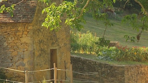 Un edificio de piedra con puerta de madera, rodeado de un muro de piedra y una cerca de cuerda.