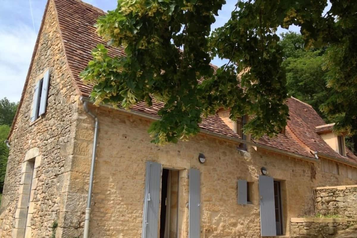 A stone building with a tiled roof, featuring a small porch and shutters on the windows.