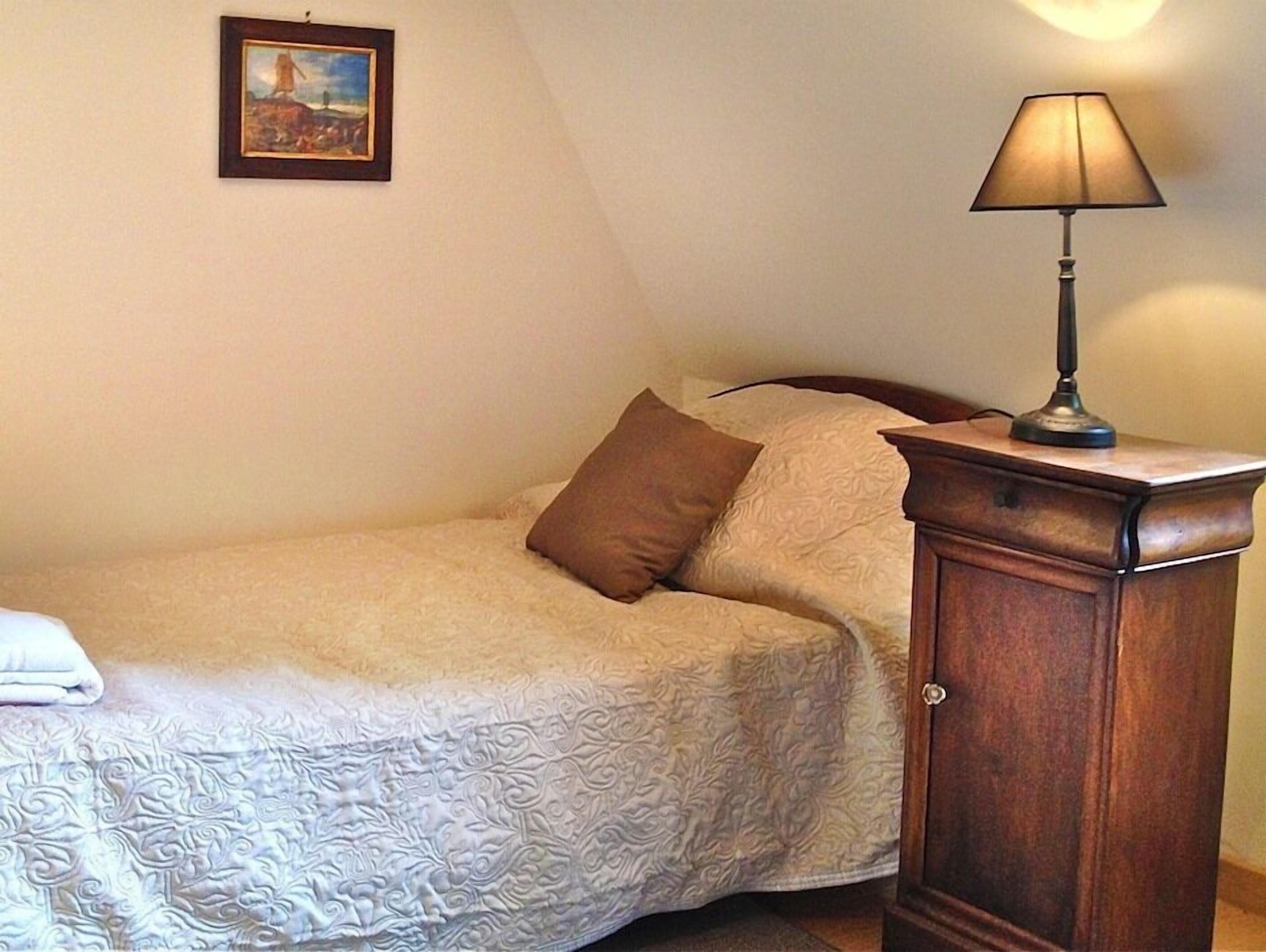 A bedroom with a bed, pillows, a lamp, and a painting on the wall.