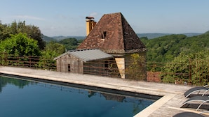 A pool area with lounge chairs and a rustic building with a sloped roof. - Tour Milou (Beynac-et-Cazenac)