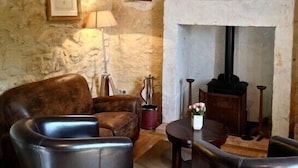 A cozy room with a stone wall, a fireplace, leather armchairs, and a small table with a vase of flowers. - Tour Milou (Beynac-et-Cazenac)