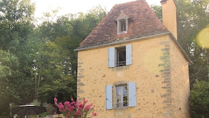 A stone-walled building with a yellow facade and blue shutters, surrounded by greenery. - Tour Milou (Beynac-et-Cazenac)