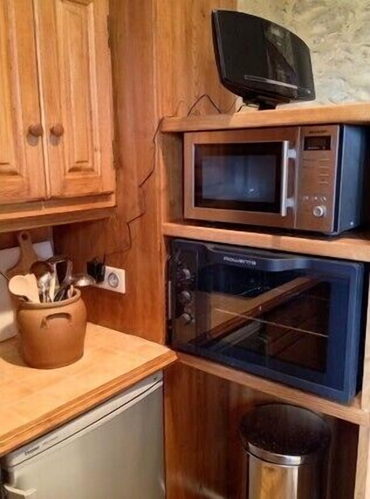 A kitchen with wooden cabinets, a microwave, an oven, and a trash bin.