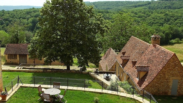 A stone building with a tiled roof, surrounded by a grassy area with a large tree. - Tour Milou (Beynac-et-Cazenac)