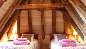 A rustic room with two beds, wooden beams, and a sloped ceiling. - Tour Milou (Beynac-et-Cazenac)