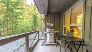 Un espace extérieur abrité, équipé d’un barbecue, de sièges et offrant une vue sur les arbres.