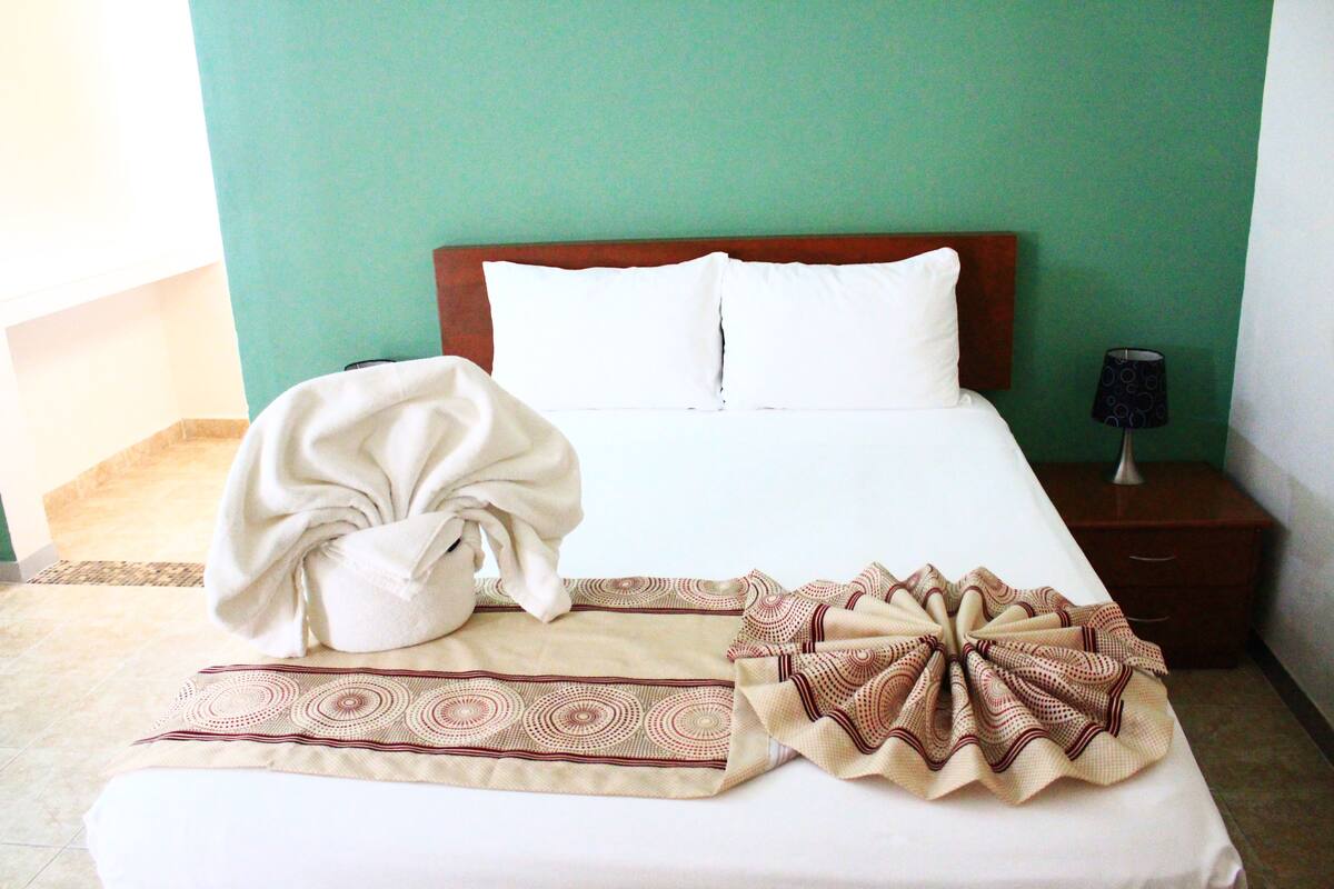 A neatly made bed with a white comforter, a beige and brown patterned throw blanket, and a white towel on the bed.