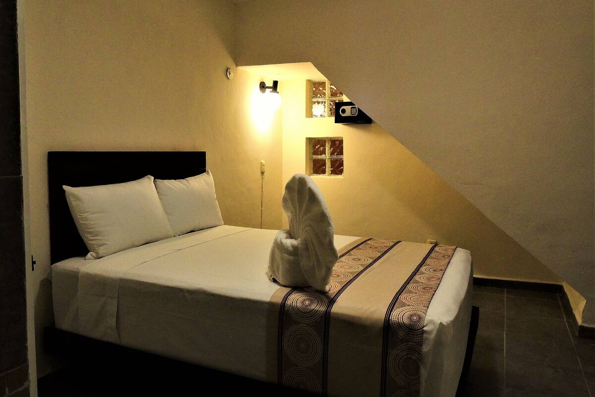 A neatly made bed with a headboard, a bedside lamp, and a small window with a view of the outside.
