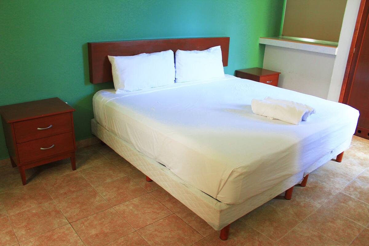 A neatly made bed with white linens, a wooden headboard, and two nightstands with drawers.