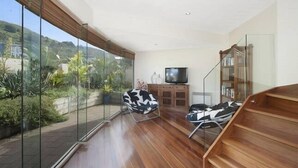 Una sala de estar moderna con un amplio ventanal, una escalera de madera y un televisor de pantalla plana.