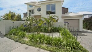 Una casa moderna de dos pisos con garaje, rodeada por un jardín bien cuidado con diversas plantas y flores.