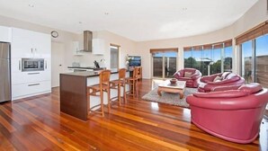 Un espacio habitable amplio con piso de madera, una mesa de comedor con sillas, un sofá rosa y una cocina al fondo.